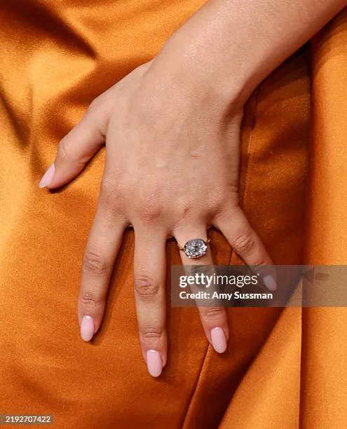 Mão de Zendaya usando anel solitário com pedra em lapidação oval sobre tecido acetinado